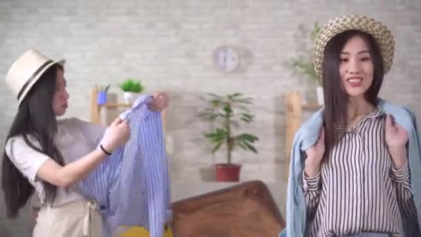 İki pozitif Asyalı kadın tatil için bavul hazırlayıp bir şeyler deniyorlar. — Stok video