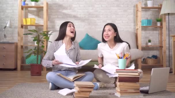 Dos estudiantes asiáticos positivos están sentados en el suelo tirando papeles — Vídeos de Stock