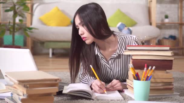 Estudante asiático cansado está se preparando para o exame deitado no chão com um laptop e livros — Vídeo de Stock