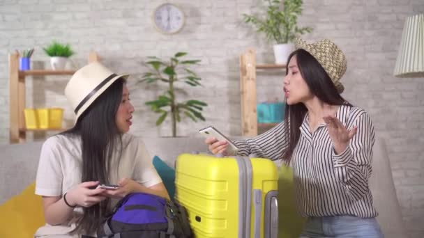 Due giovani donne asiatiche deluse si siedono in soggiorno con valigie per le vacanze — Video Stock