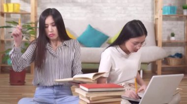 Ders kitapları ve dizüstü bilgisayarı olan iki yorgun Asyalı öğrenci yerde oturuyor.