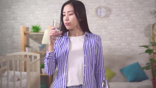 Молодая азиатка пьет из стакана и недовольна качеством воды — стоковое видео
