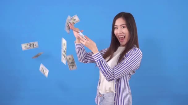 Young beautiful asian woman scatters paper banknotes dollars on a blue background slow mo — Stock Video