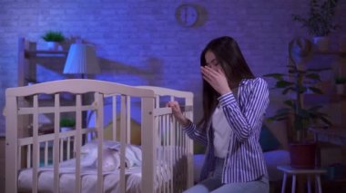 Uykulu genç Asyalı anne bir bebek karyolası sallıyor.