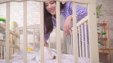 Olumlu genç Asyalı anne beşikte bebekle konuşuyor.