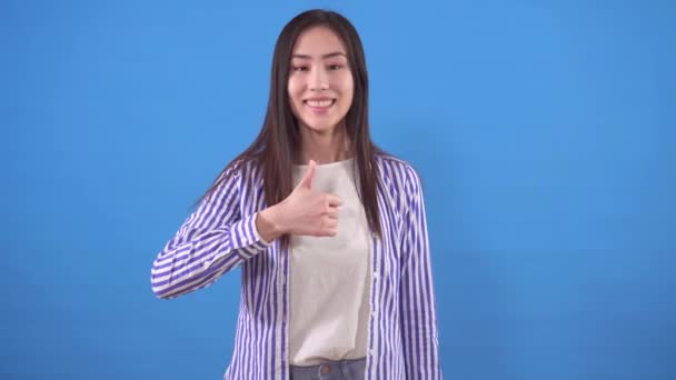 Positivo joven asiático mujer muestra un thumbs arriba en un azul fondo — Vídeo de stock