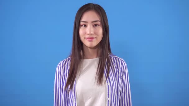 Portrait of a young asian woman in a shirt stands on a blue background — Stock Video