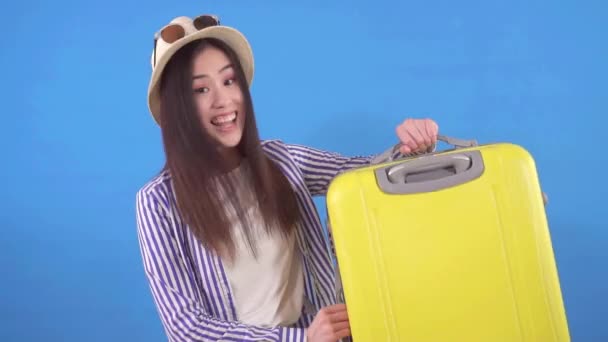 Young asian tourist after a vacation with a suitcase on a blue background slow mo — Stock Video