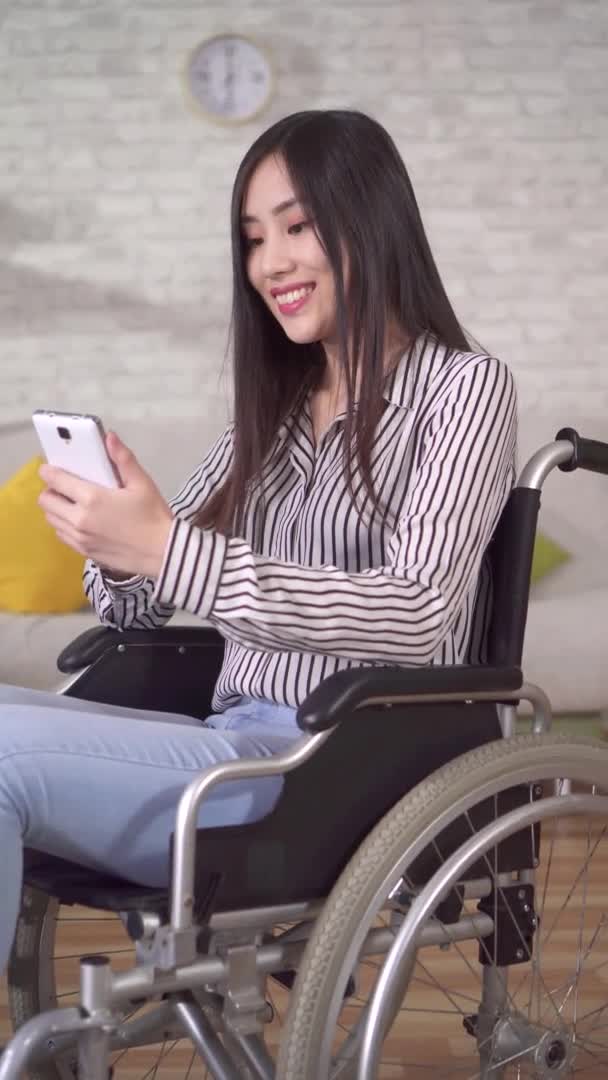 휠체어를 타고 있는 아시아의 젊은 장애 여성 이 스마트폰을 이용하고 있다. — 비디오