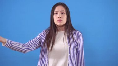 Gömlekli genç Asyalı kadın avucunun içini mavi bir fonda gezdiriyor.