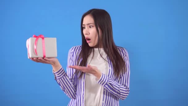 푸른 배경에 있는 작은 선물에 불만을 품은 한 젊은 동양 여자 — 비디오