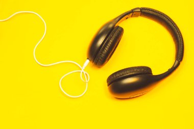 Sarı arka planda beyaz kablo olan siyah kulaklıklar. modern kulaklıklar
