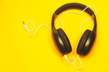 Sarı arka planda beyaz kablo olan siyah kulaklıklar. modern kulaklıklar