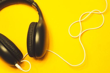 Sarı arka planda beyaz kablo olan siyah kulaklıklar. modern kulaklıklar