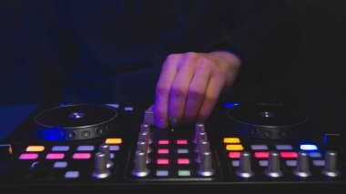 DJ müzik çalıyor. Ses karıştırıcı kontrolörü, düğmeleri ve sürgüleri var. Karanlığın içinde elleri ve pikapları aydınlatılmış kontrollerle karıştırın.