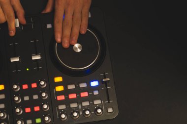 DJ müzik çalıyor. Ses karıştırıcı kontrolörü, düğmeleri ve sürgüleri var. Karanlığın içinde elleri ve pikapları aydınlatılmış kontrollerle karıştırın.