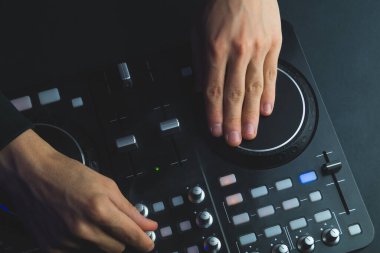 DJ müzik çalıyor. Ses karıştırıcı kontrolörü, düğmeleri ve sürgüleri var. Karanlığın içinde parlayan kontrollü pikaplarla karıştırma güvertesinde.