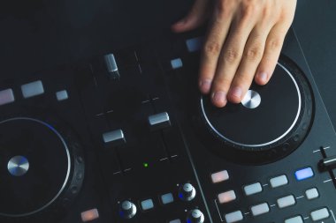 DJ müzik çalıyor. Ses karıştırıcı kontrolörü, düğmeleri ve sürgüleri var. Karanlığın içinde parlayan kontrollü pikaplarla karıştırma güvertesinde.