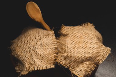 Koyu arkaplanda ahşap kaşıkla keten kumaşlı bal kapları.