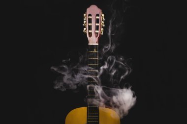 Siyah arka planda duman içinde bir gitar. Akustik müzik aleti. gitar ensesinde teller