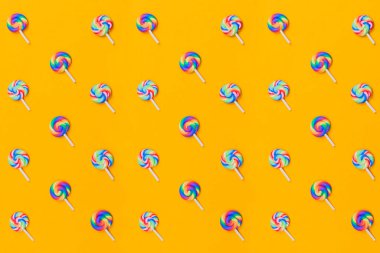 Lolipoplar sıraya dizildi. sarmal şeker desenli. Sarı arka planda bir sürü tatlı var. Şekerlerle süslenmiş şenlik