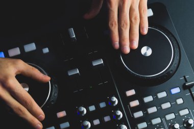 DJ müzik çalıyor. Ses karıştırıcı kontrolörü, düğmeleri ve sürgüleri var. Karanlığın içinde parlayan kontrollü pikaplarla karıştırma güvertesinde.