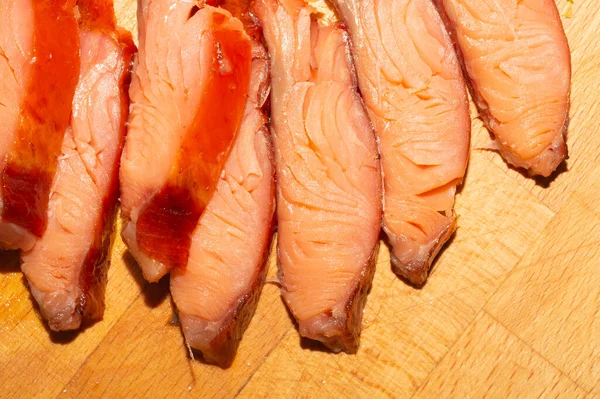 Kırmızı balık parçaları yaklaşıyor. Tütsülenmiş somon. Tahta bir masada deniz ürünleri.