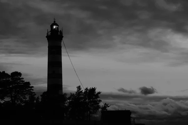 Deniz feneri kulesi, dramatik bir gökyüzü ile karanlıkta parlar. Karanlıkta parlayan fenerin silueti