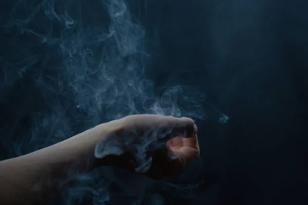 Elde sigara içmek. Karanlıkta soyut sis. El bir büyü yaratır.