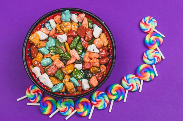 Mor arka planda lolipoplar. Renkli taşlar şeklinde şekerleme kasesi. Renkli şekerler