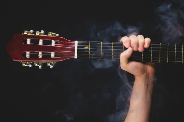 Hand holds acoustic guitar. musical instrument on black background