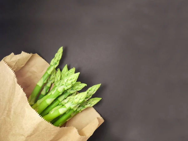 Surowe szparagi w papierowej torbie. Świeże zielone szparagi wczarnym tle — Zdjęcie stockowe