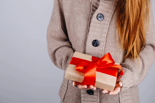 Woman in knitted sweater holding a present, Gift is packed in craft paper with pine cones and tied with red ribbon. DIY way to wrap a present. Selective focus.