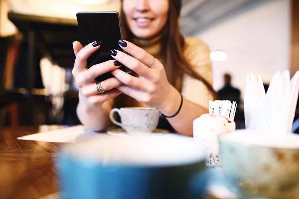 Woman typing text message on smart phone in a cafe. Cropped image of young woman sitting at a table with a coffee using mobile phone. Toned. Selective focus. — Stock Photo, Image