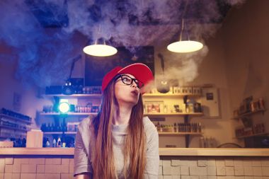 Genç kadın kırmızı bere duman elektronik sigara vape dükkanında güzel.