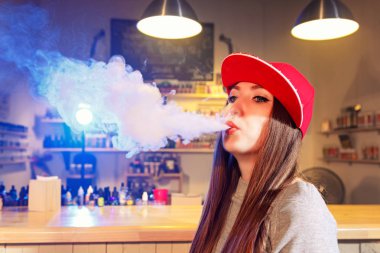 Genç kadın kırmızı bere duman elektronik sigara vape dükkanında güzel.