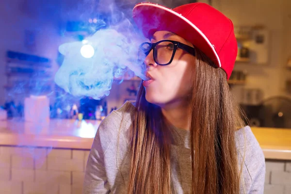 Jeune jolie femme en bonnet rouge fume une cigarette électronique à la boutique de vape — Photo