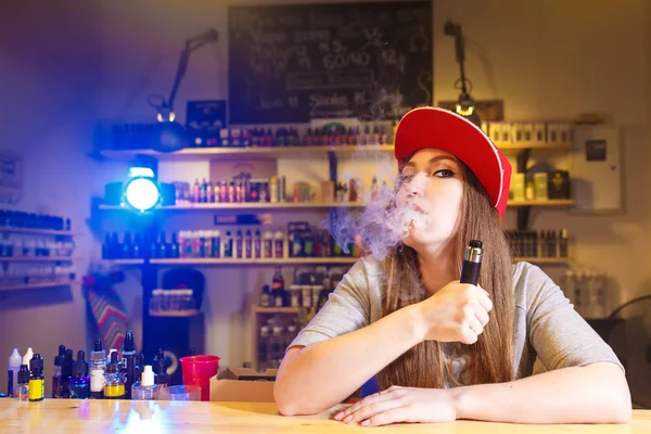 Gadis cantik bertopi merah merokok rokok elektronik di toko vape — Stok Foto