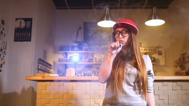 Ung söt kvinna i röd mössa rök en elektronisk cigarett på vape shop. Närbild. — Stockvideo