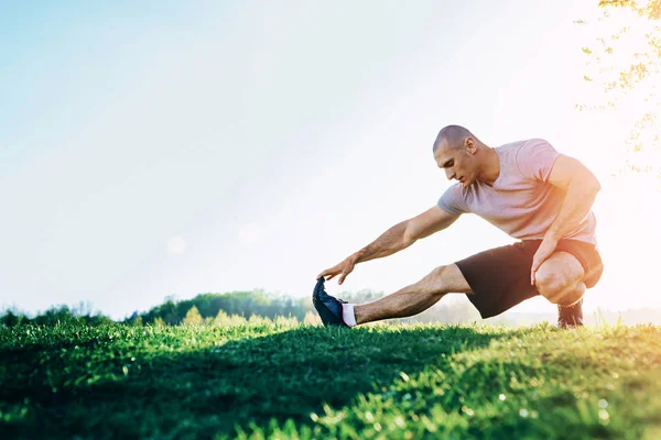 Fiatal sportos futó nyújtó feladatot, felkészülés edzés a parkban. naplemente — Stock Fotó