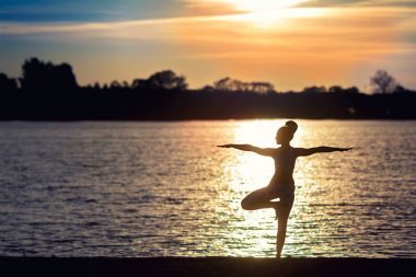 Genç kadının gün batımında yoga egzersizleri Gölü sahilde yapması