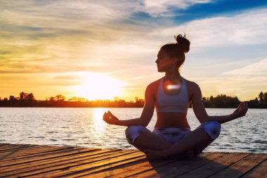 Genç kadının gün batımında yoga egzersizleri Gölü sahilde yapması