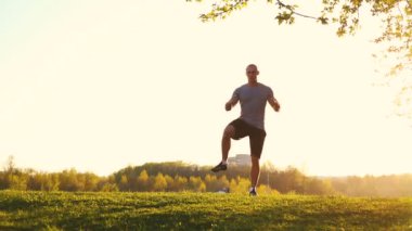 parkta egzersiz için hazırlanıyor germe egzersiz yaparak genç atletik atlet. gün batımı, tonda video