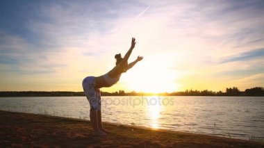 Genç kadının gün batımında yoga egzersizleri Gölü sahilde yapması