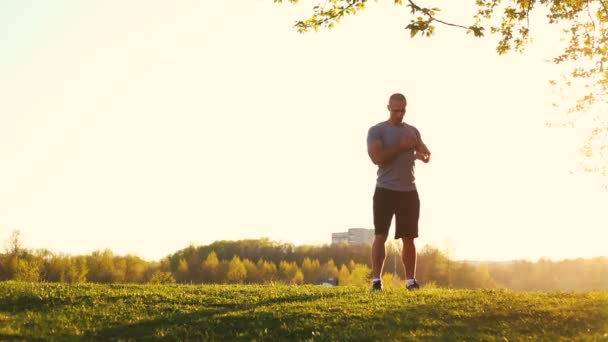 Jonge sportieve loper doen stretching oefening, voorbereiding op training in het park. zonsondergang, getinte video — Stockvideo