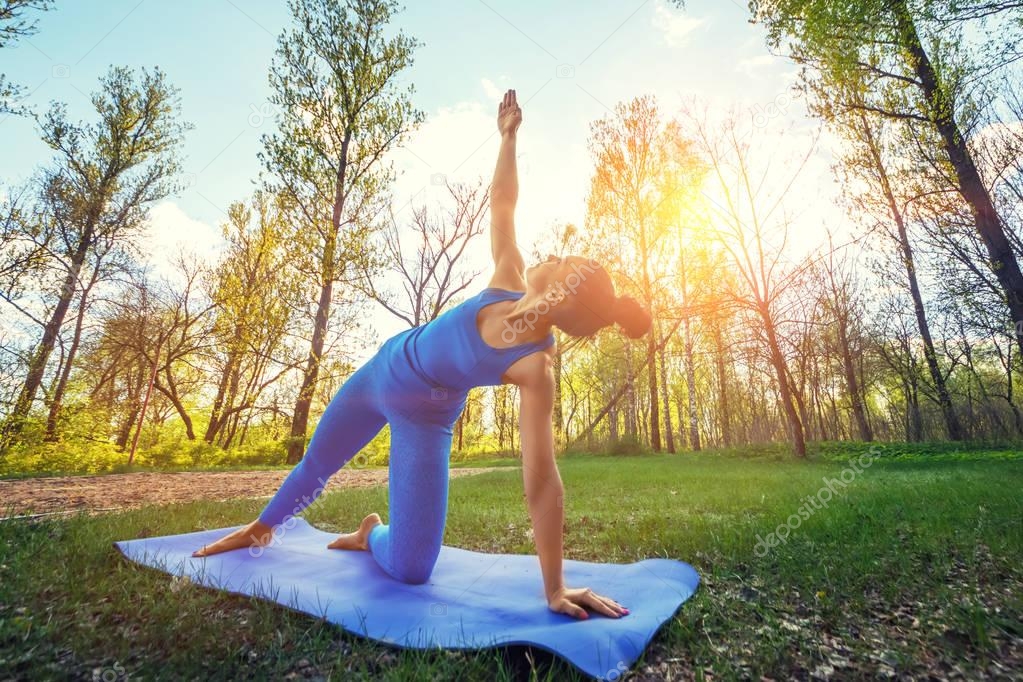 Young woman doing yoga exercises in the summer city park. Health lifestyle concept.