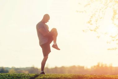 parkta egzersiz için hazırlanıyor germe egzersiz yaparak genç atletik atlet. günbatımı