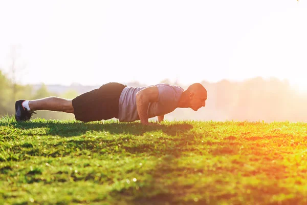 Sport. Sportoló csinál fekvőtámaszokat a naplemente a parkban. Izmos srác gyakorlása. — Stock Fotó