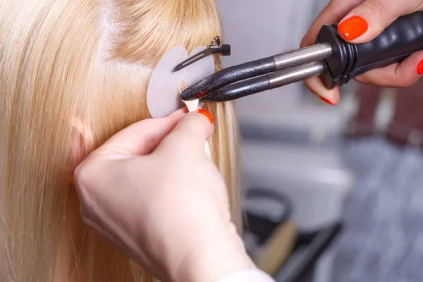 Procedimento de extensões de cabelo. Cabeleireiro faz extensões de cabelo para menina, loira em um salão de beleza. Foco seletivo . — Fotografia de Stock