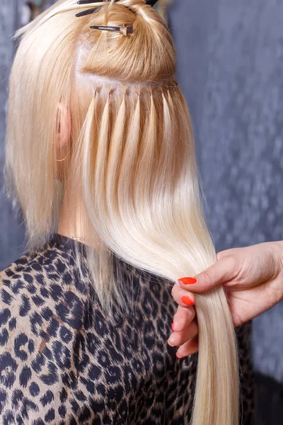 Hår extensions förfarande. Frisören gör hårförlängningar till ung flicka, Blond i en skönhetssalong. Selektivt fokus. — Stockfoto